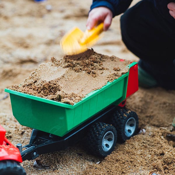 Child playing with toy dumptruck of sand